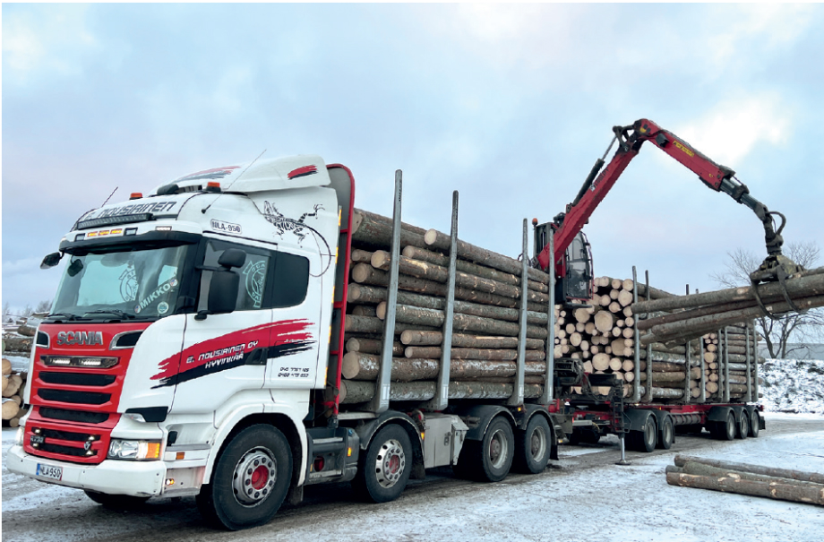 Utilaj de tip macara care folosește brațul mecanic pentru a așeza bușteni în remorca unui tir.